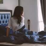 Người phụ nữ ngồi một mình trong quán cà phê đông người, tay cầm điện thoại, ánh mắt xa xăm, thể hiện sự cô đơn giữa đám đông ảo.