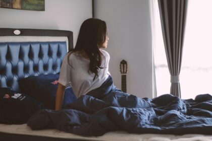 Người phụ nữ ngồi một mình trong quán cà phê đông người, tay cầm điện thoại, ánh mắt xa xăm, thể hiện sự cô đơn giữa đám đông ảo.