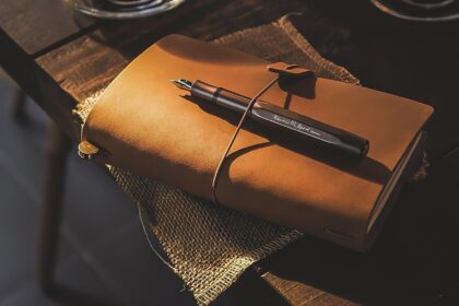 Người phụ nữ ngồi trên bàn làm việc lộn xộn, nhìn ra ngoài cửa sổ với vẻ mặt trầm tư, biểu tượng cho vòng luẩn quẩn trì hoãn và sự khó khăn trong việc thoát khỏi chu trình thói quen.